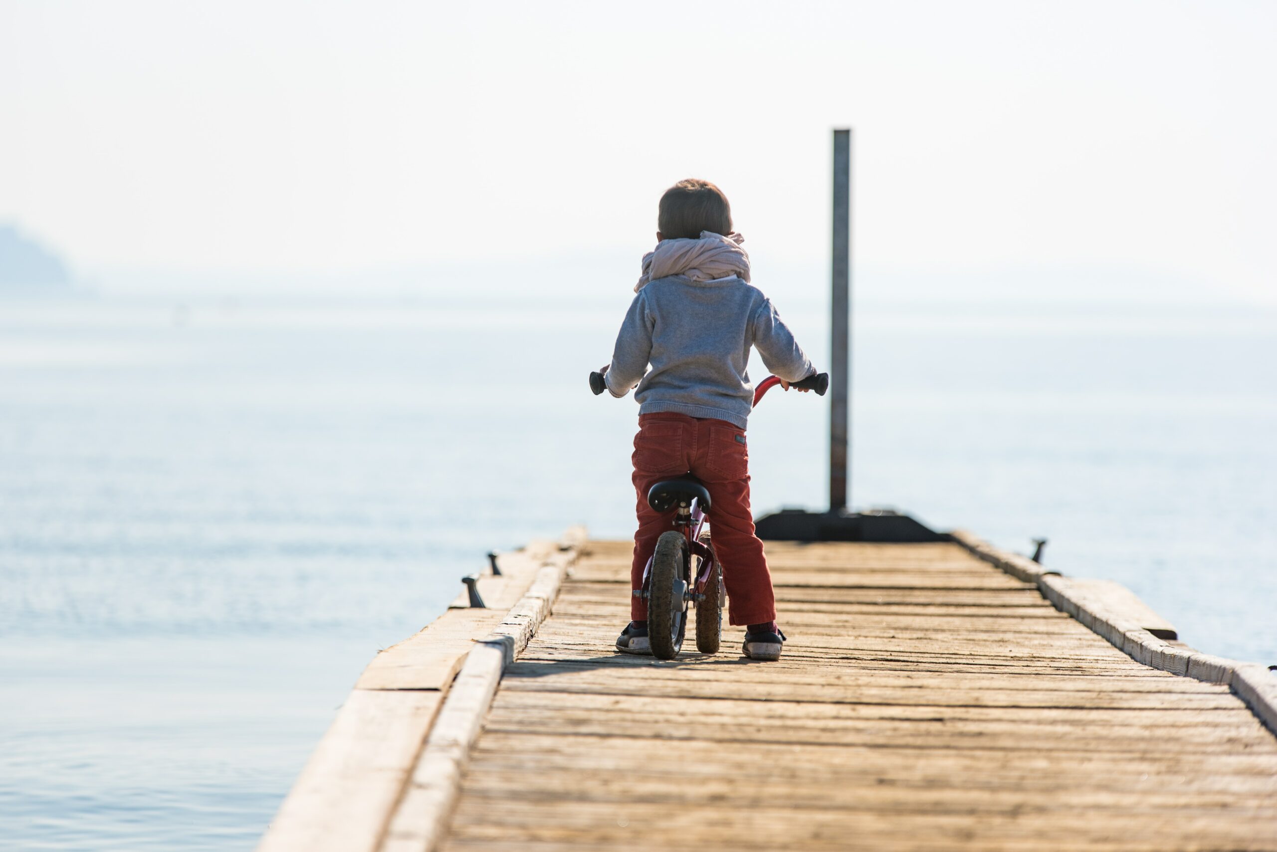 A child on a dock with a bicycle near the ocean.