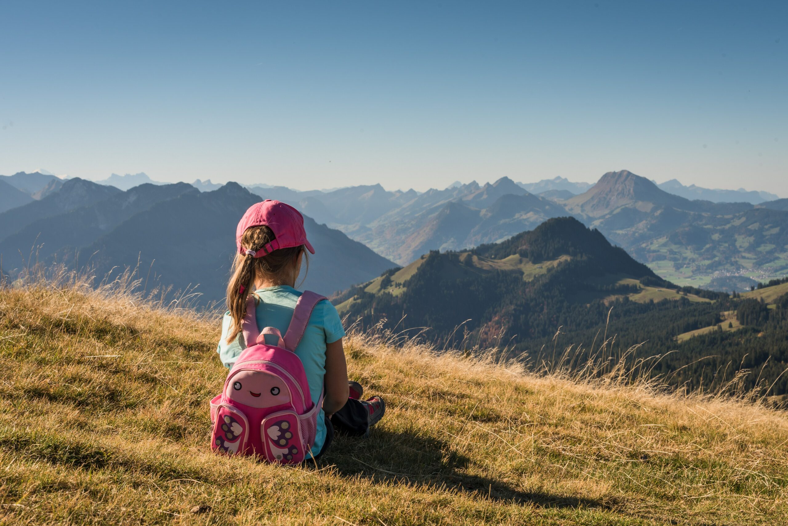 A young girl with pink hiking backpack. Sitting in the mountains.