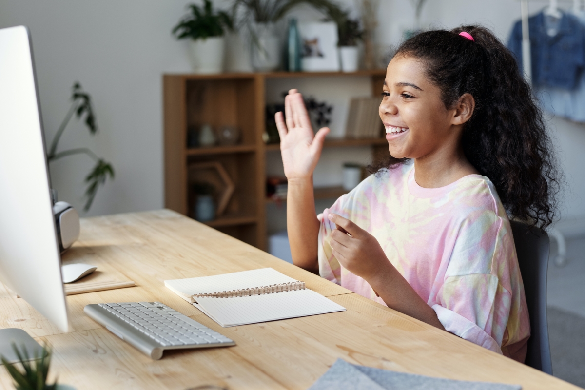 Child doing online school, raising hand in front of computer