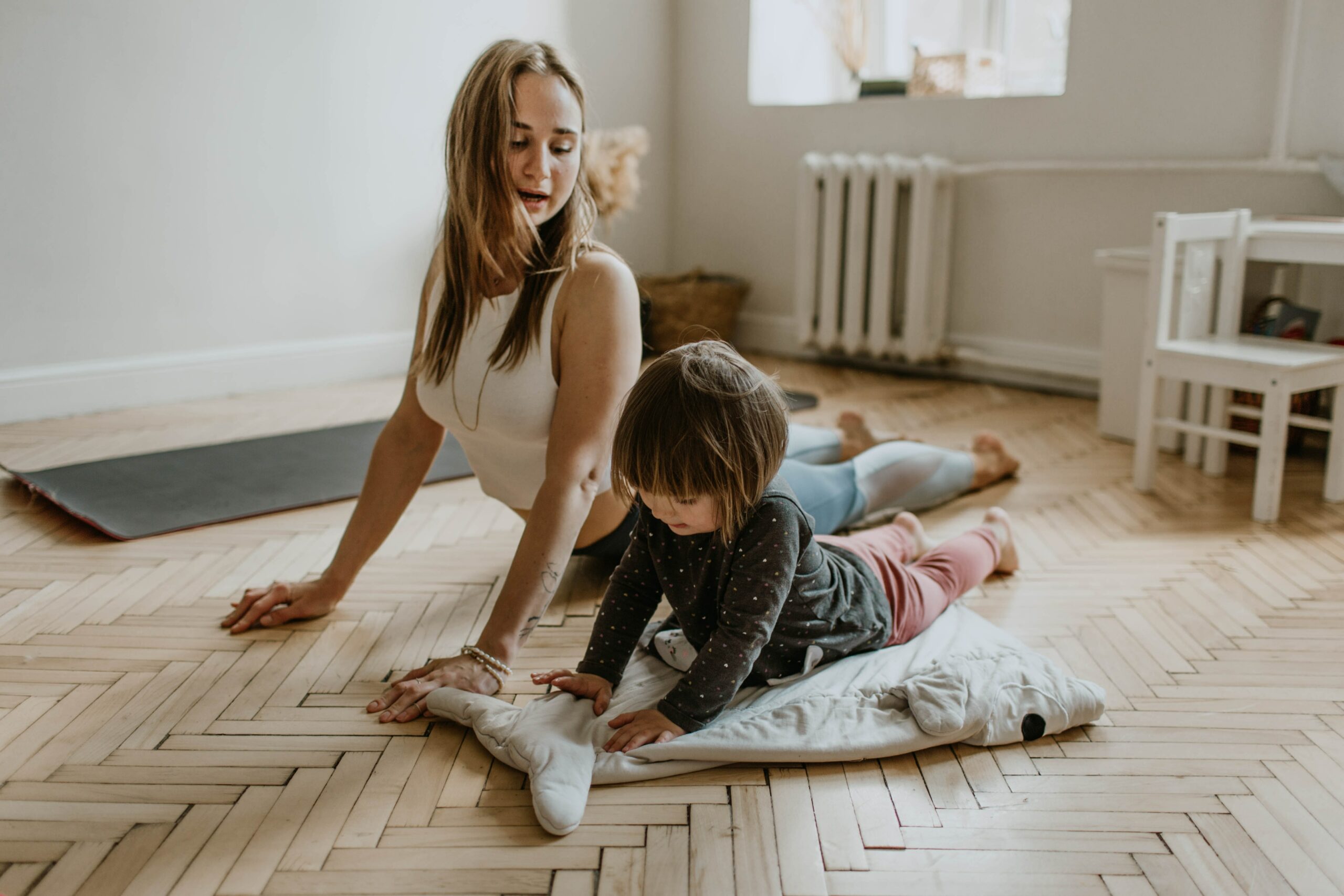 A mom and toddler doing yoga on the floor. Yoga is an inexpensive sport to participate in.