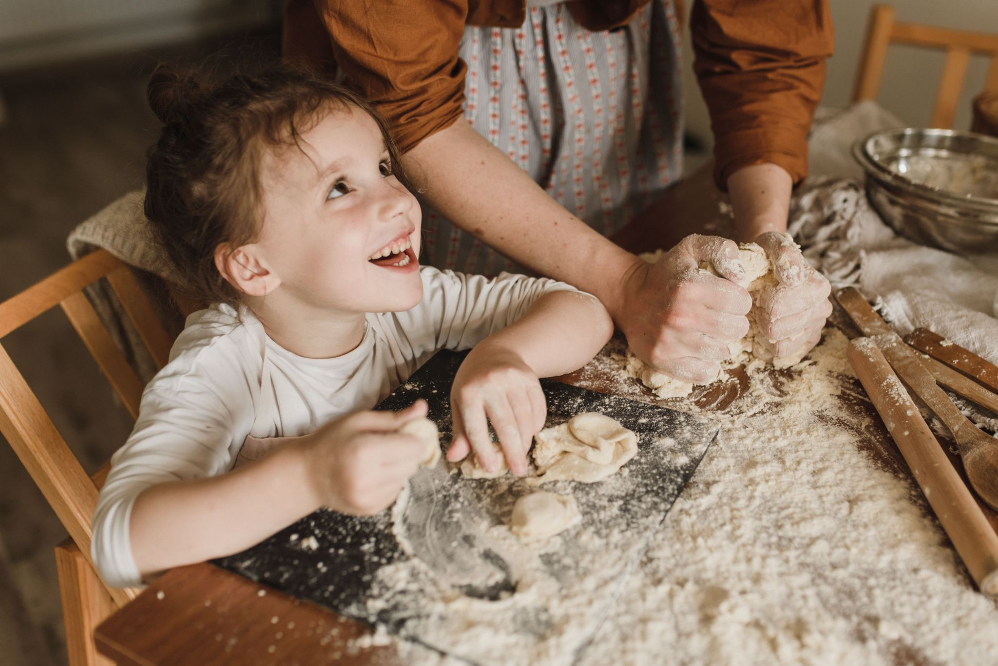 Little Girl with parent with flour on table making dough