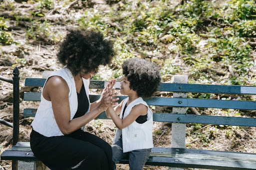 A mother smiling as she talks with her child sitting outside on a park bench.