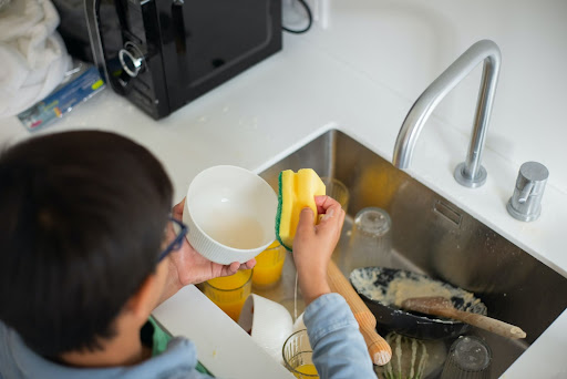 A child washing the dishes helps to build confidence and self-esteem.