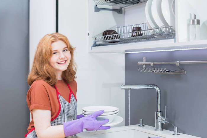 A teen girl working in a restaurant washing dishes - part time job